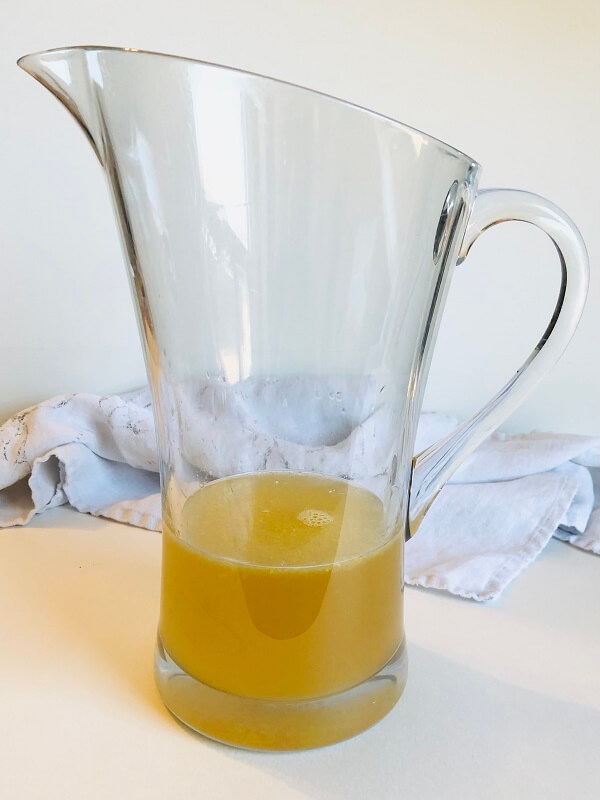 A large lucite pitcher with yellow liquid inside.