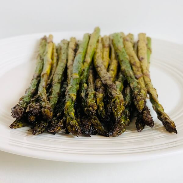A pile of roasted asparagus on a white round plate.