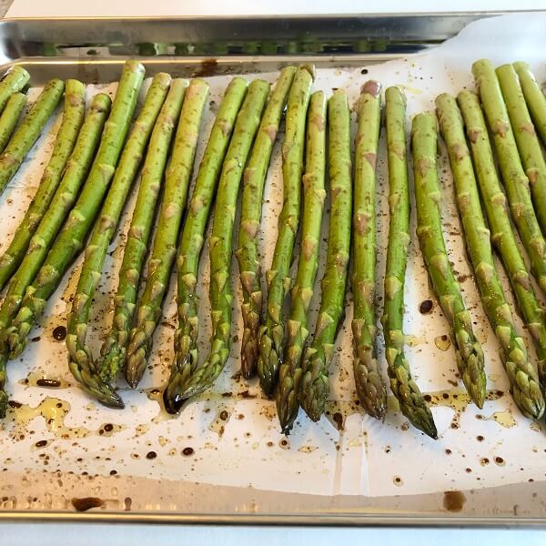 Raw asparagus on a parchment paper lined sheet pan.