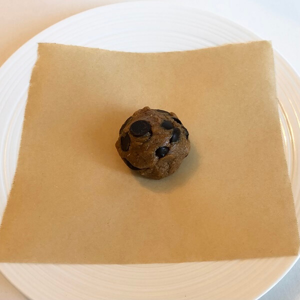 A cookie dough ball on a square of paper on a plate.