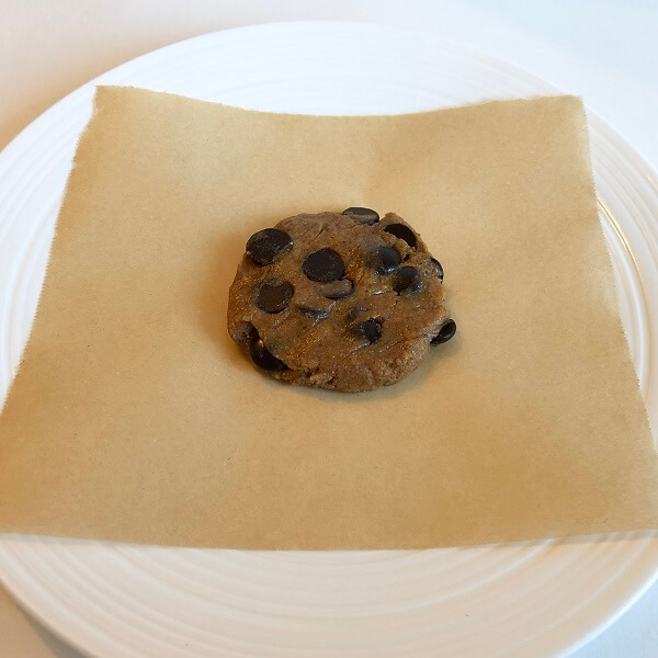 A raw cookie on a square of parchment paper on a plate.