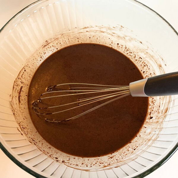 Cupcake ingredients being mixed in a glass bowl with a whisk.