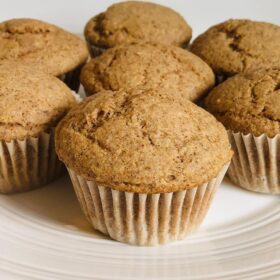 Seven brown muffins on a white plate.