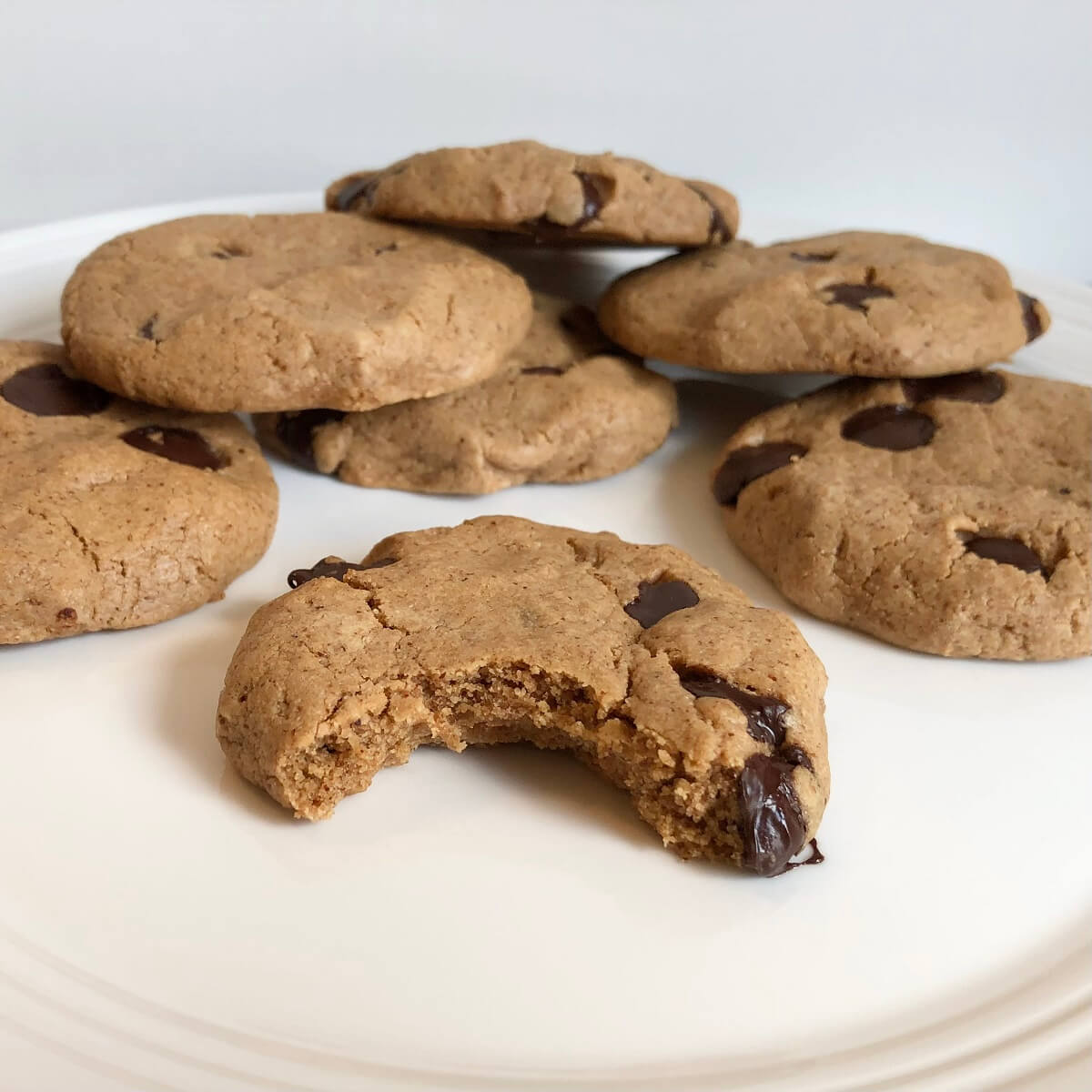 Maple syrup chocolate chip cookies piled on a white plate with a bite missing from one.