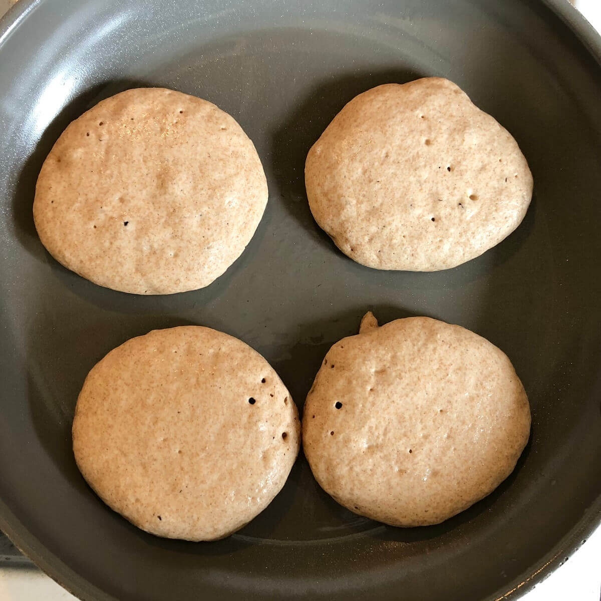 Four pancakes cooking in a frying pan.