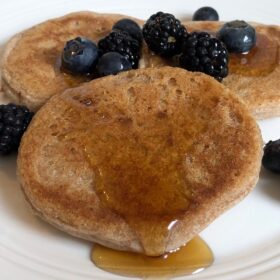Three pancakes with berries and syrup on a white plate.