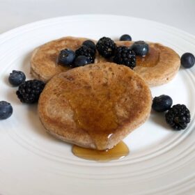 Three pancakes on a plate with fruit and syrup.