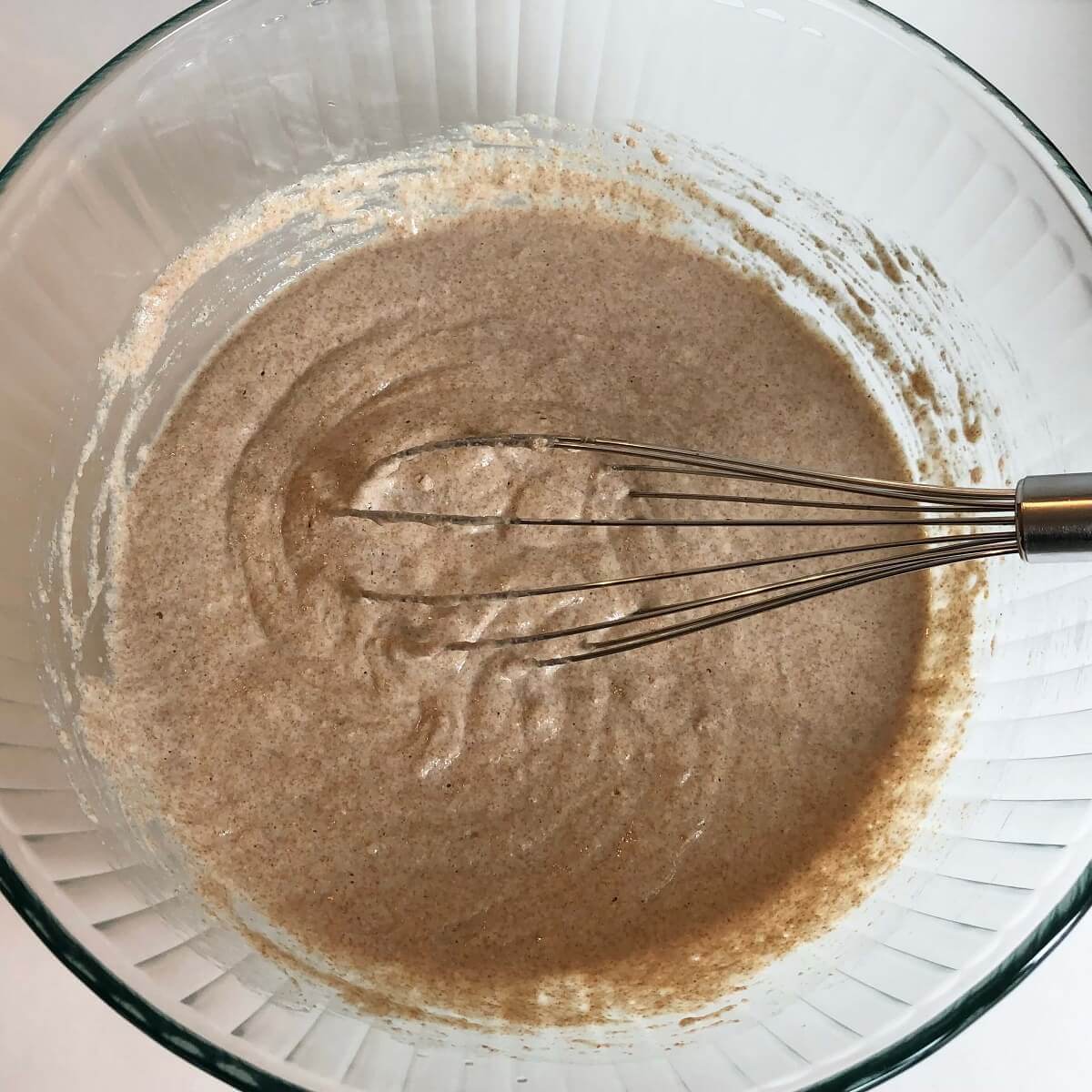 Pancake batter in a glass mixing bowl with a whisk.