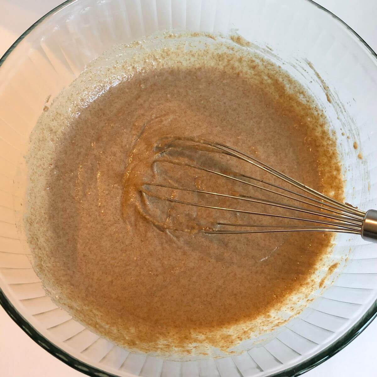 Spelt batter in a glass bowl with a whisk.