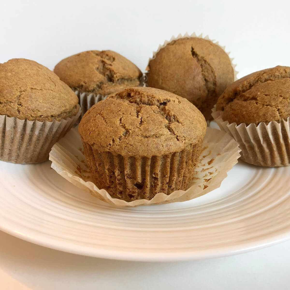 Five spelt muffins on a white plate.