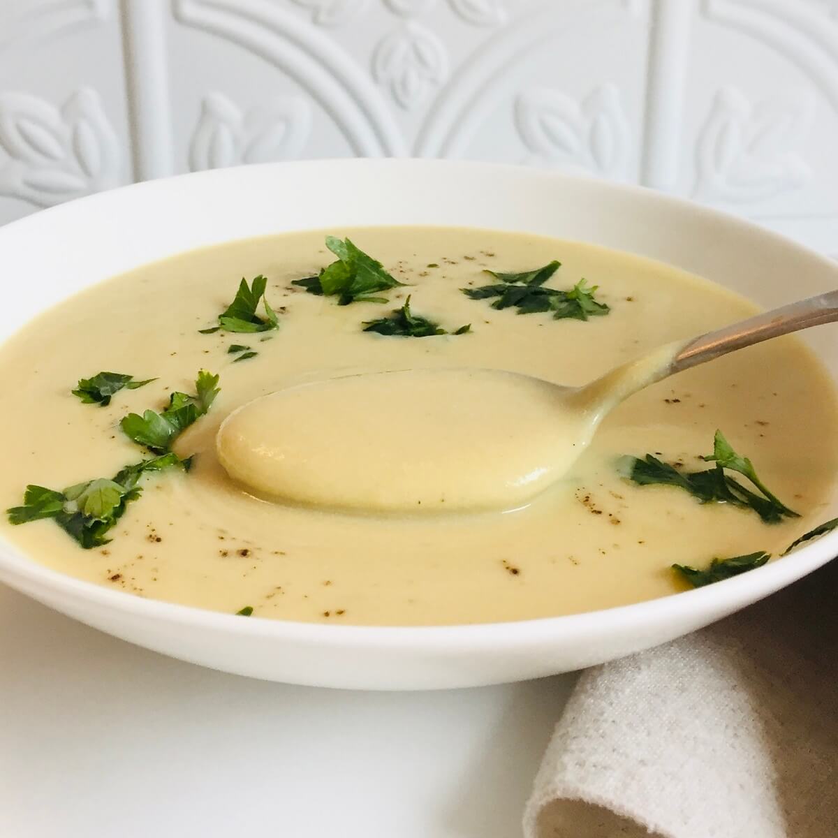 A bowl of vegan cream of cauliflower soup with parsley sprinkled on top.