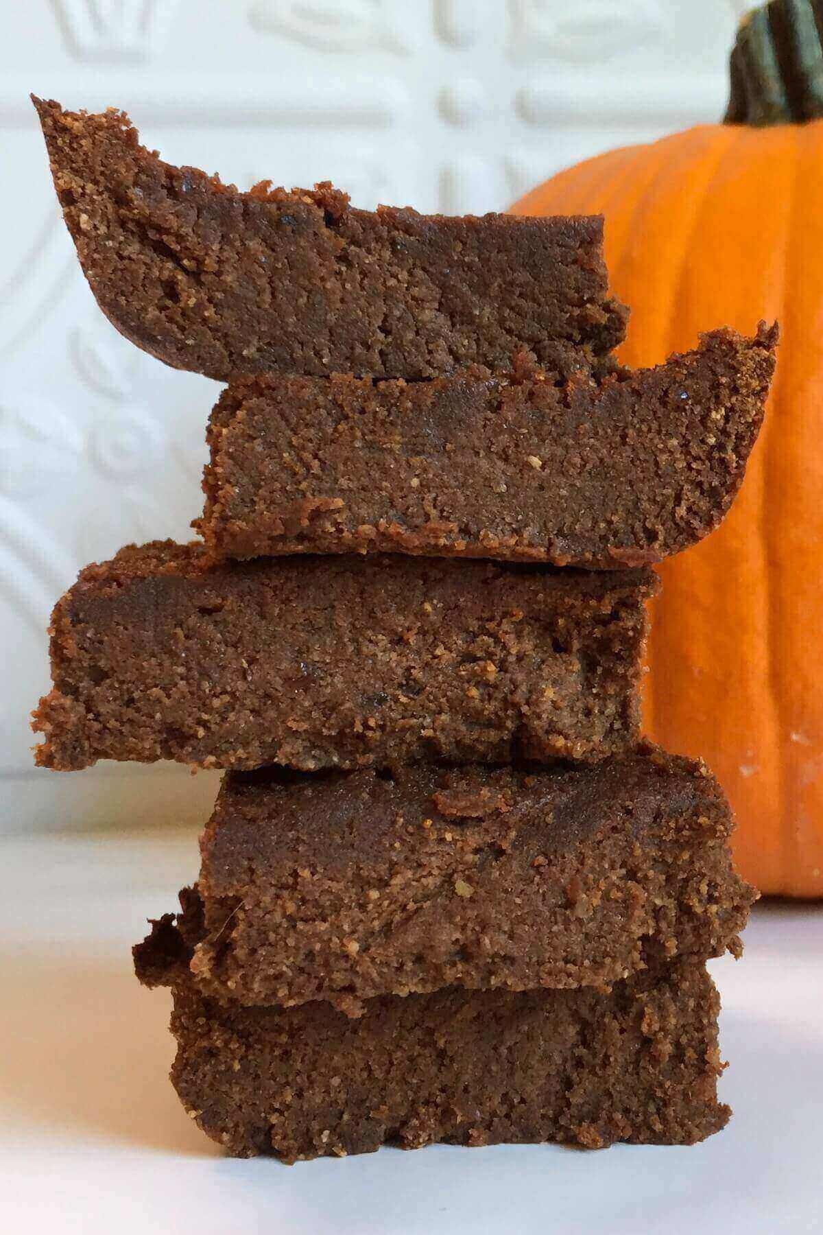 Five brownies next to a pumpkin.