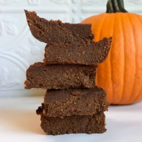 Vegan pumpkin brownies stacked next to a pumpkin.