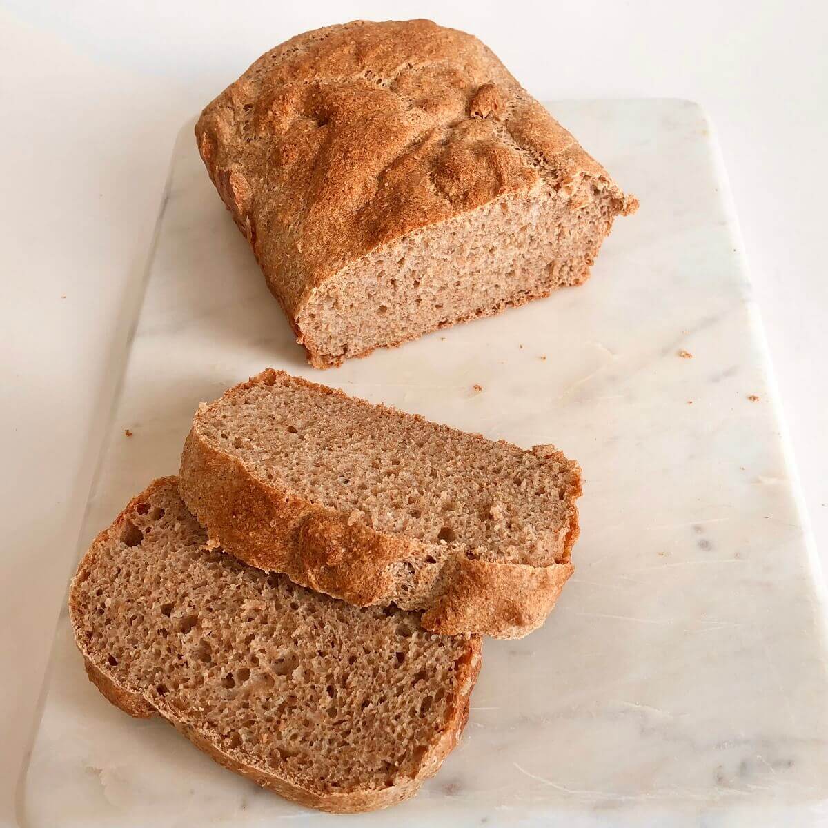 A loaf of vegan whole wheat bread on a marble cutting board with slices cut.