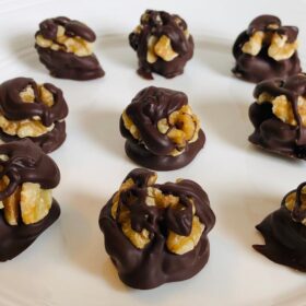 Chocolate dipped walnuts on a white plate.