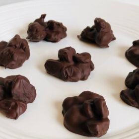 Chocolate coated cherries on a white plate.