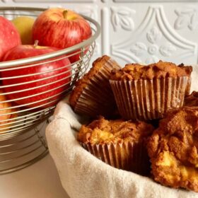 Coconut flour apple muffins next to a wire basket full of apples.