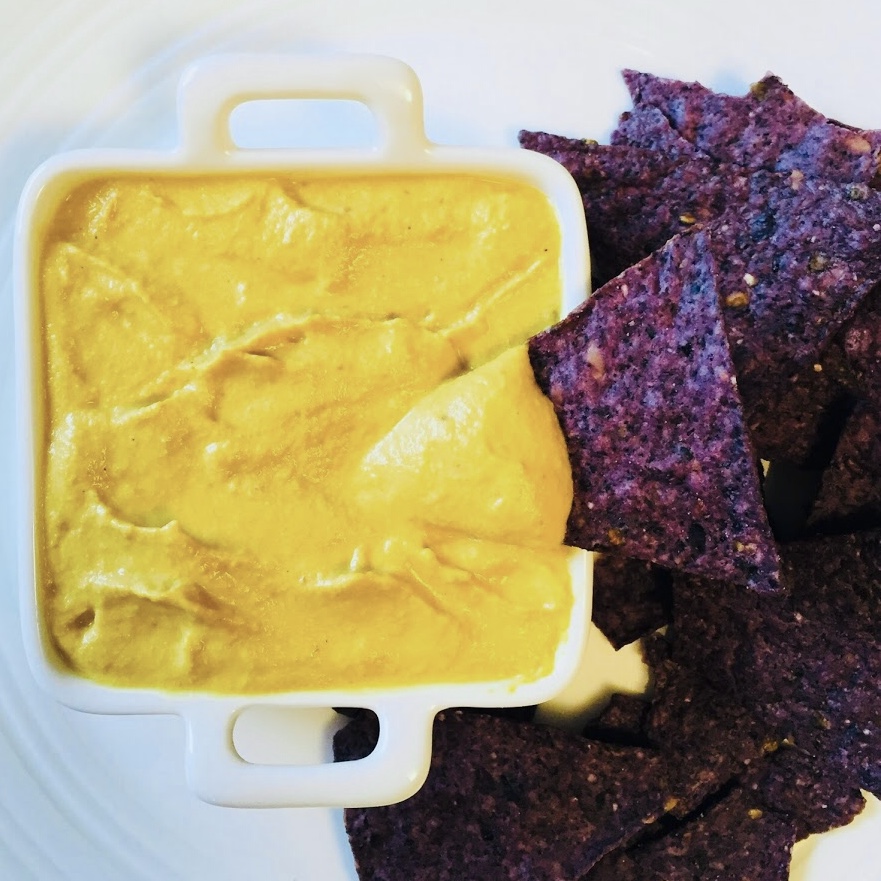 Cheese sauce and blue corn chips on a plate.