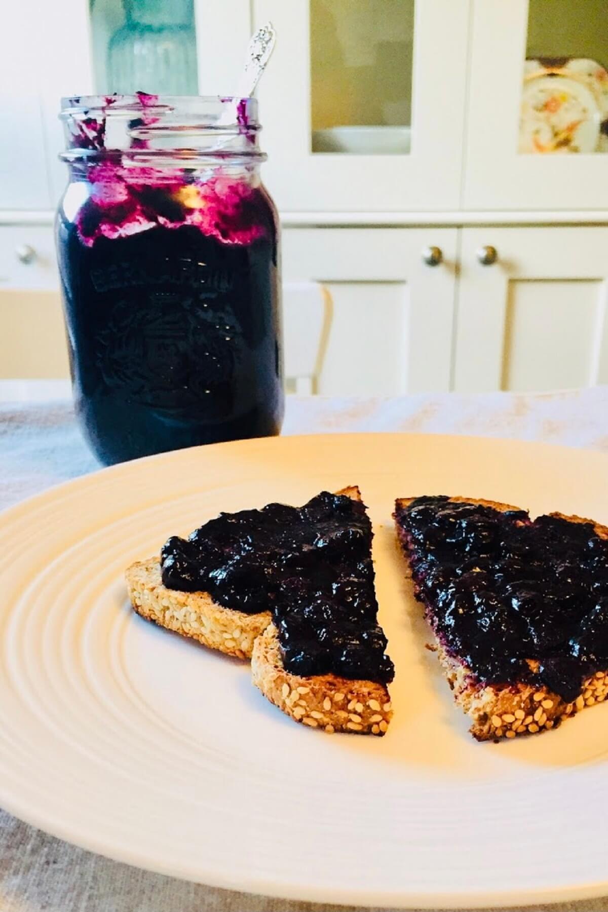 A jar of blueberry freezer jam next to some toast with jam spread on it.