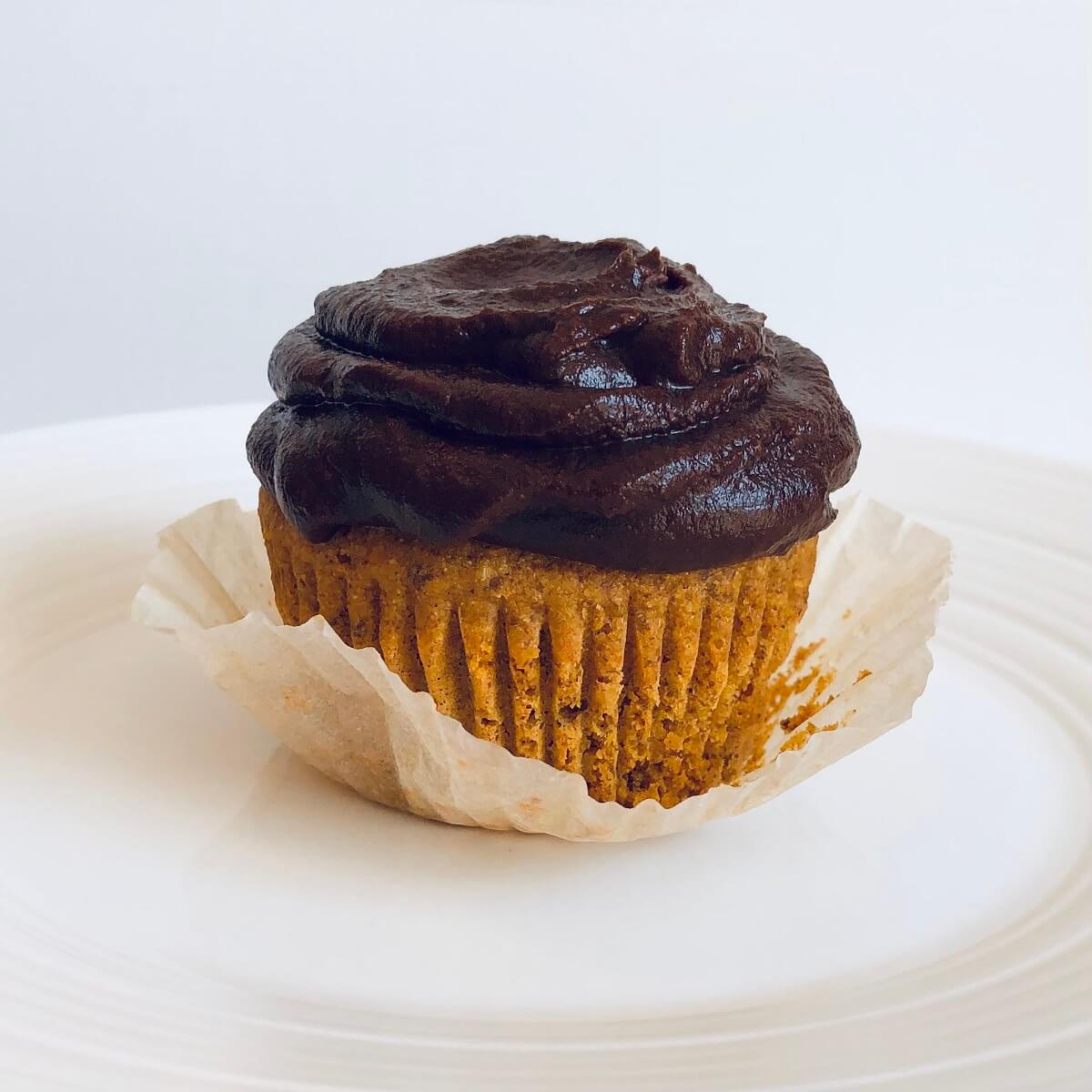 A cupcake with chocolate frosting on a white plate.