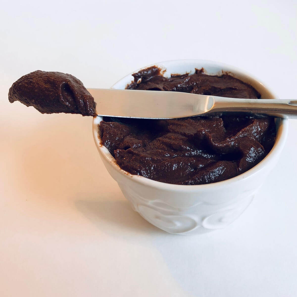 A dollop of frosting on a butter knife resting on top of a bowl of frosting.