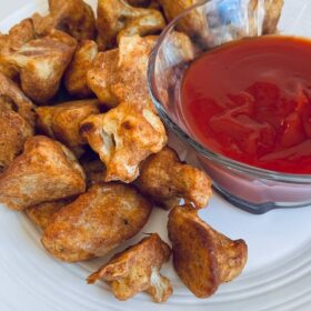Baked cauliflower pieces on a plate next to a dish of ketchup.