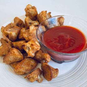 Crispy baked cauliflower bites on a plate next to a glass bowl filled with ketchup.