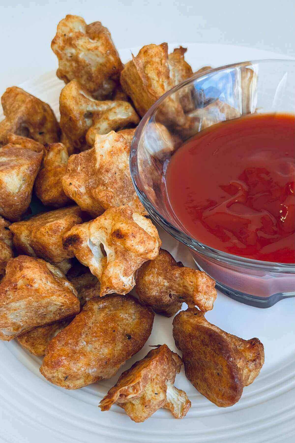 Crispy cauliflower on a plate next to a bowl of red sauce.