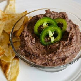 A glass bowl filled with bean dip next to a pile of chips.