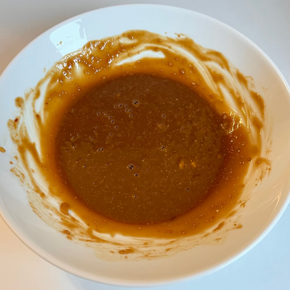 Thick brown marinade in a white bowl.