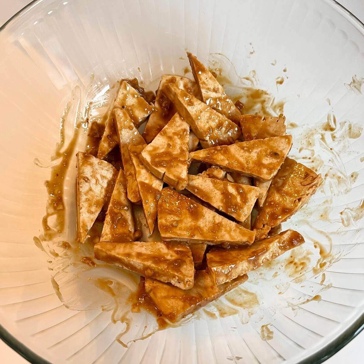 Tofu marinating in a large glass bowl.