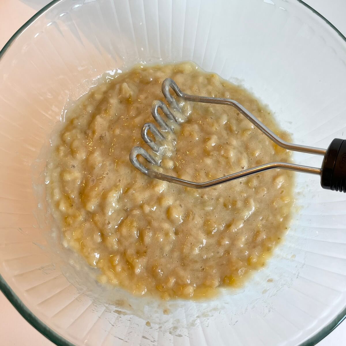 Mashed bananas in a large glass mixing bowl.