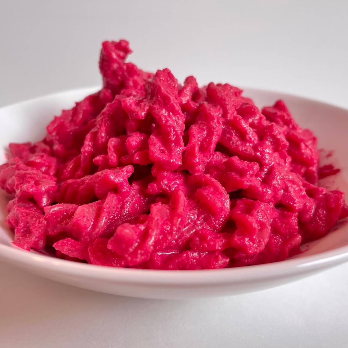 A dish of noodles covered in a pink beet pasta sauce.