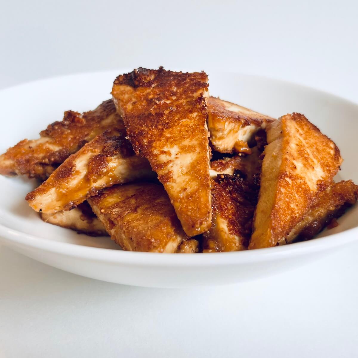 Triangular cut cooked, marinated tofu pieces in a bowl.