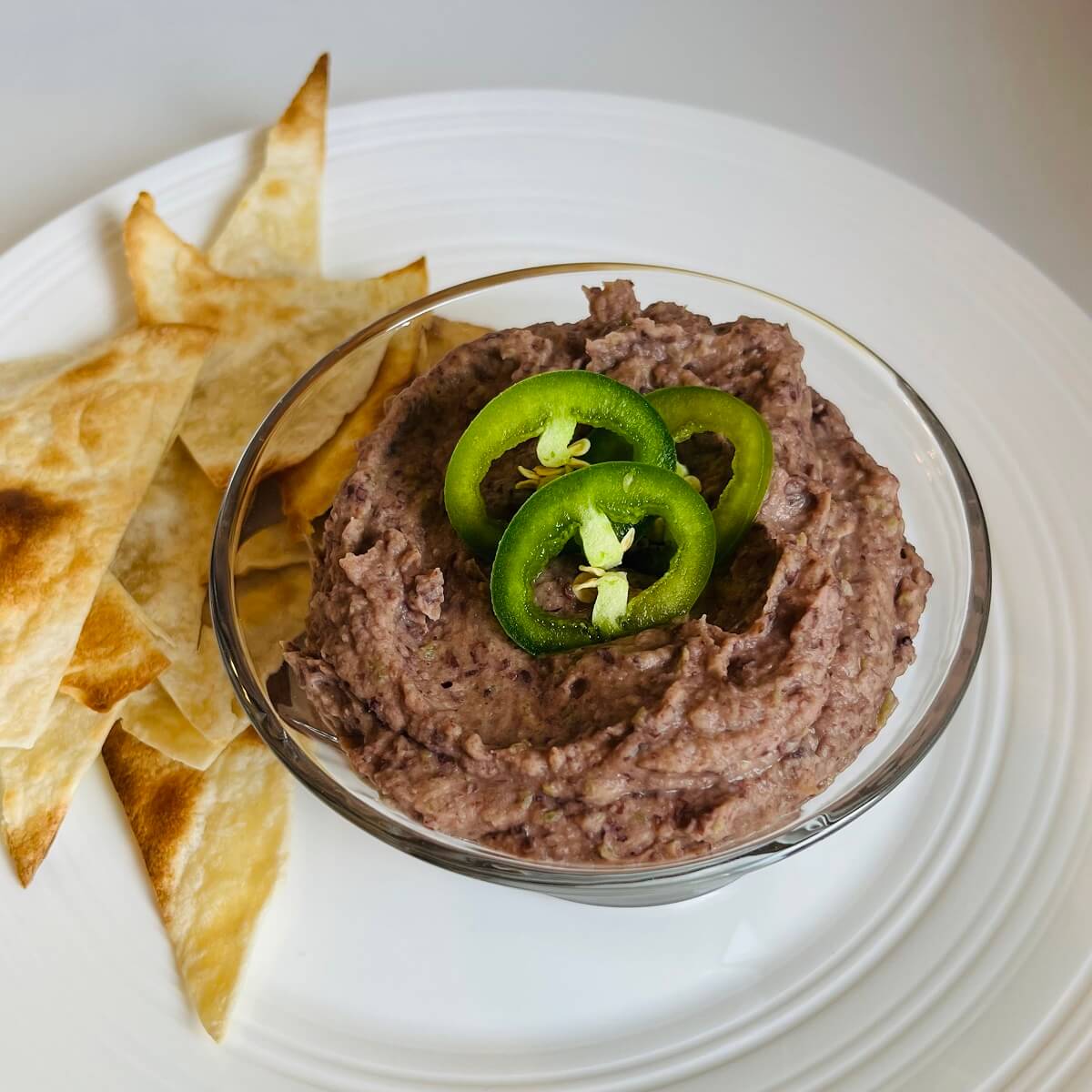 Vegan black bean dip in a glass bowl next to some tortilla chips.