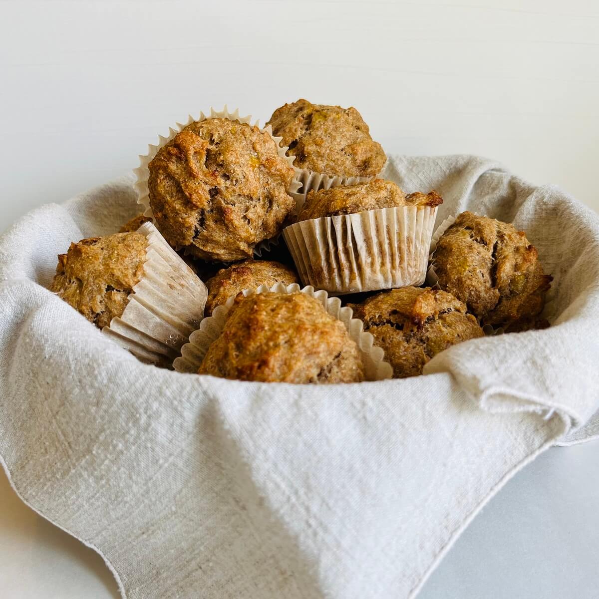 Whole wheat banana muffins piled in a basket lined with a linen napkin.