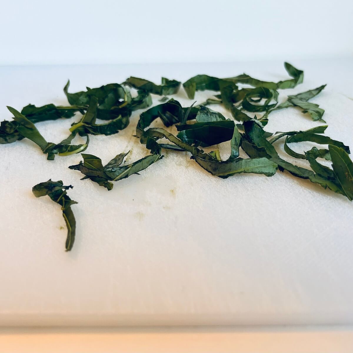 Basil cut in strips on a white cutting board.