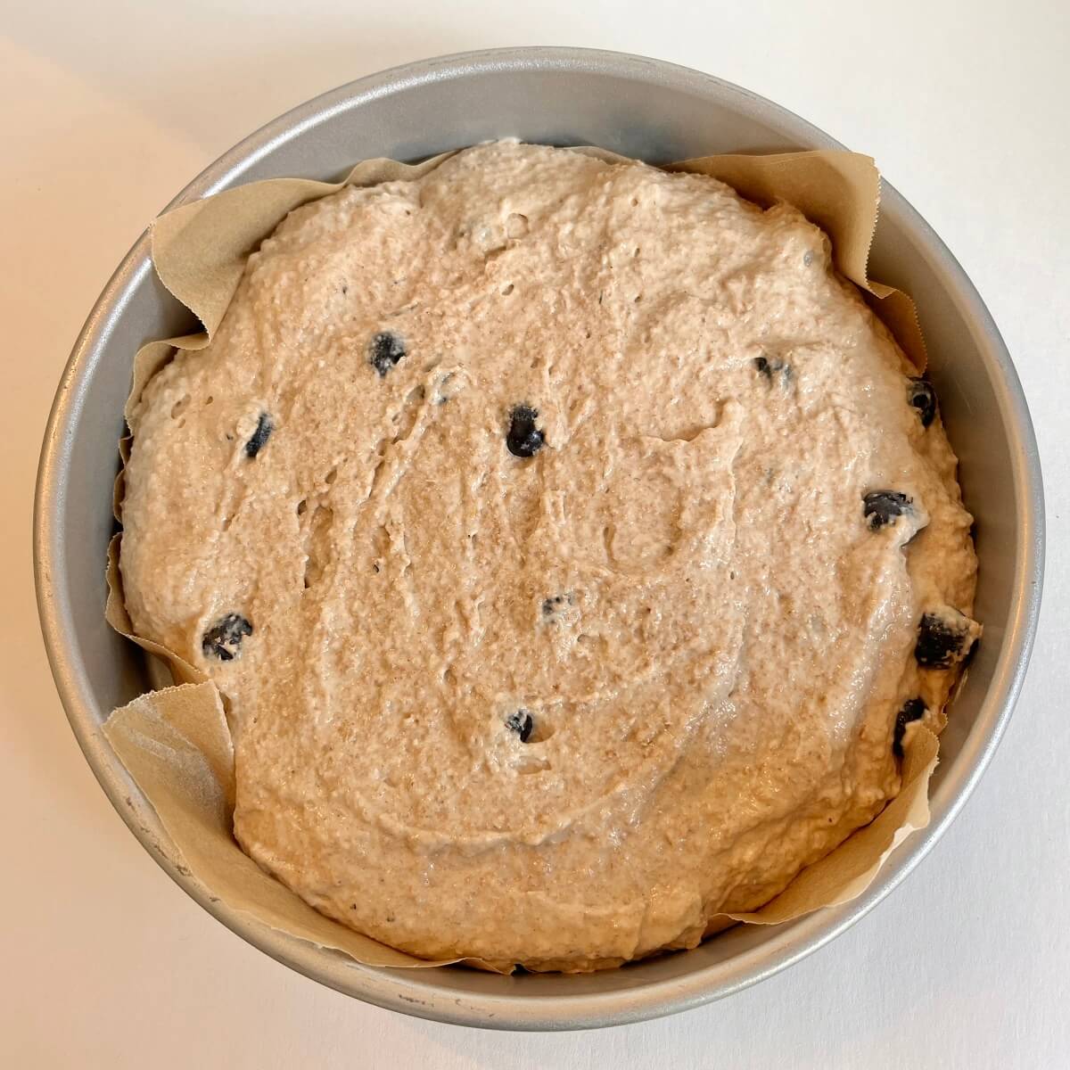 Raw cake batter in a round metal baking pan.