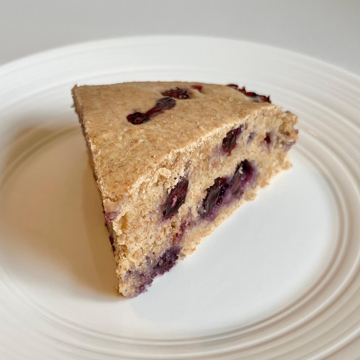 A thick slice of vegan berry cake on a white plate.