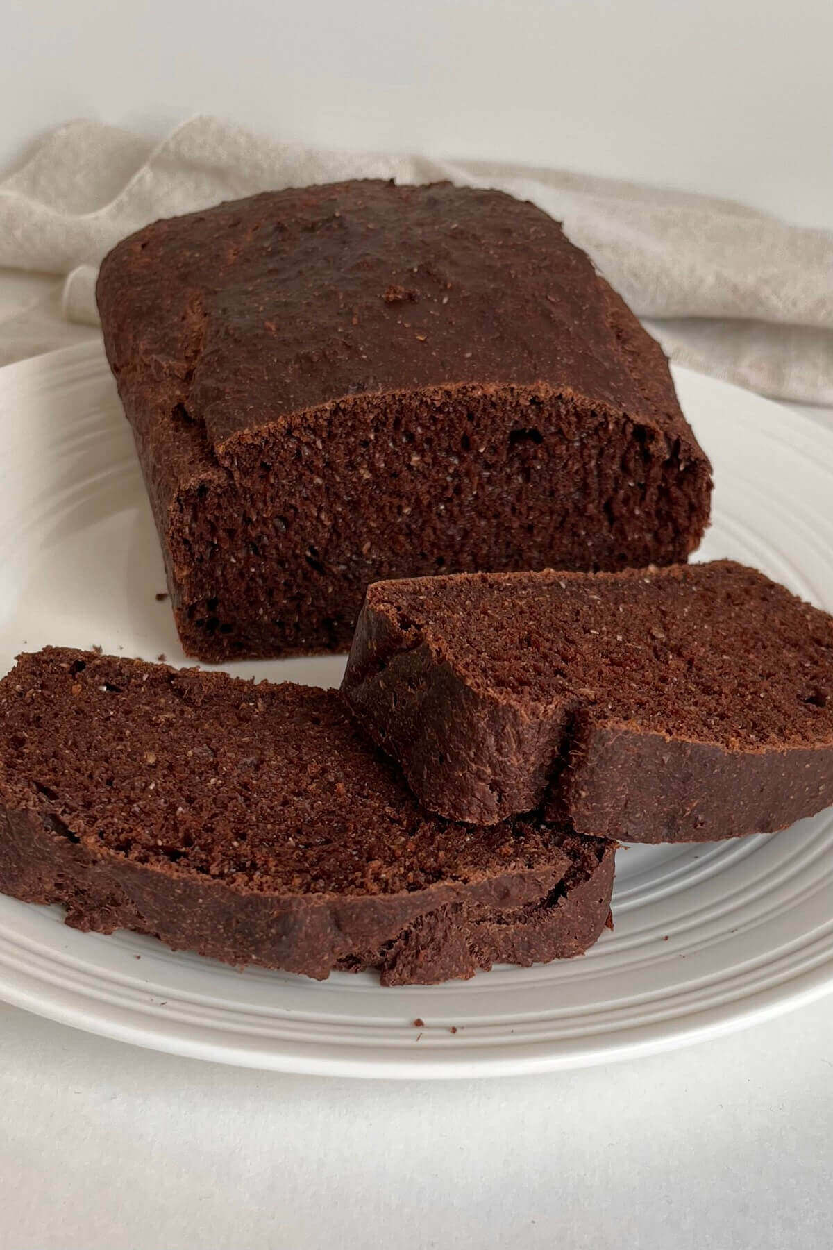 A loaf of brown bread with two slices cut on a white plate.