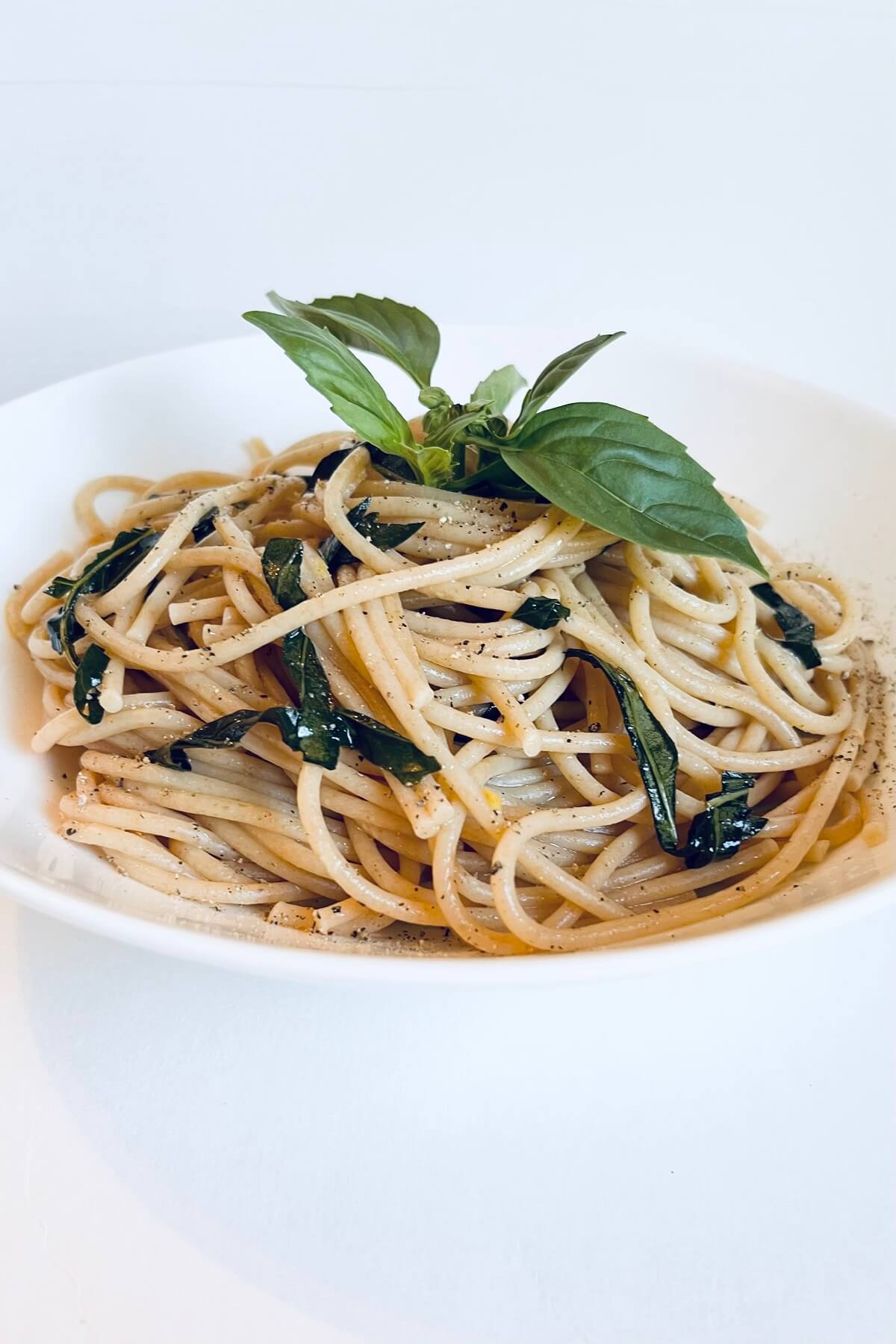 A bowl filled with pasta garnished with a sprig of basil.
