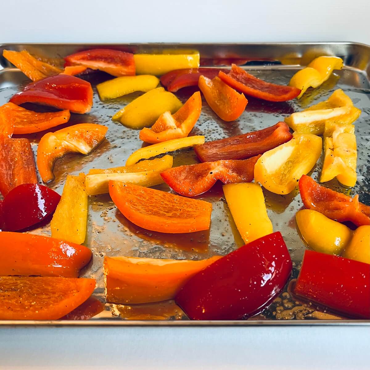 Peppers tossed with oil and spices on a sheet pan.