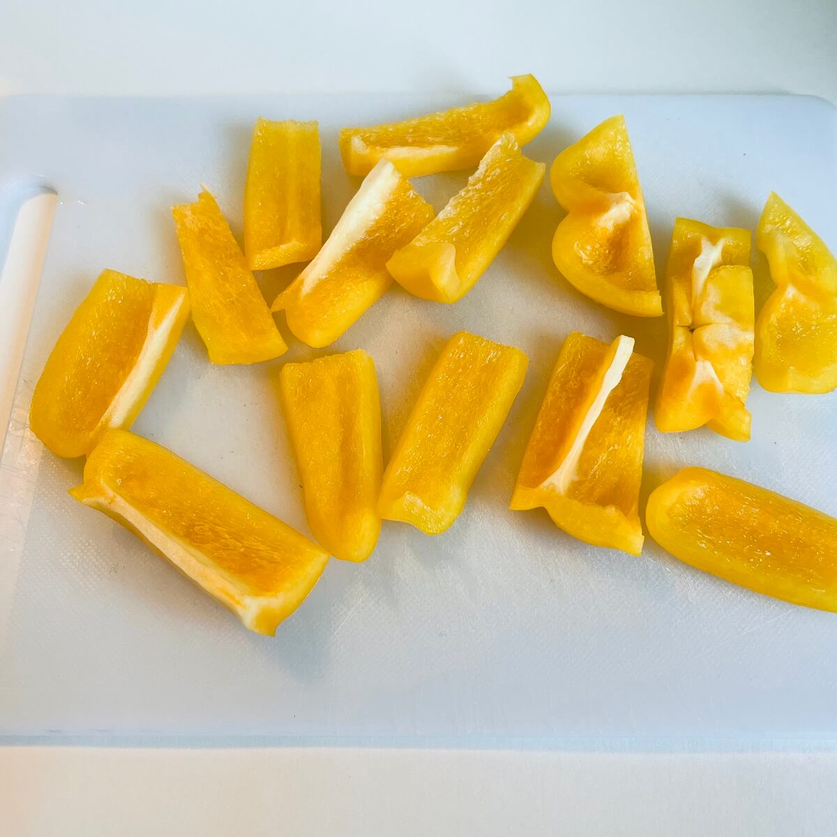 Sliced yellow peppers on a white cutting board.