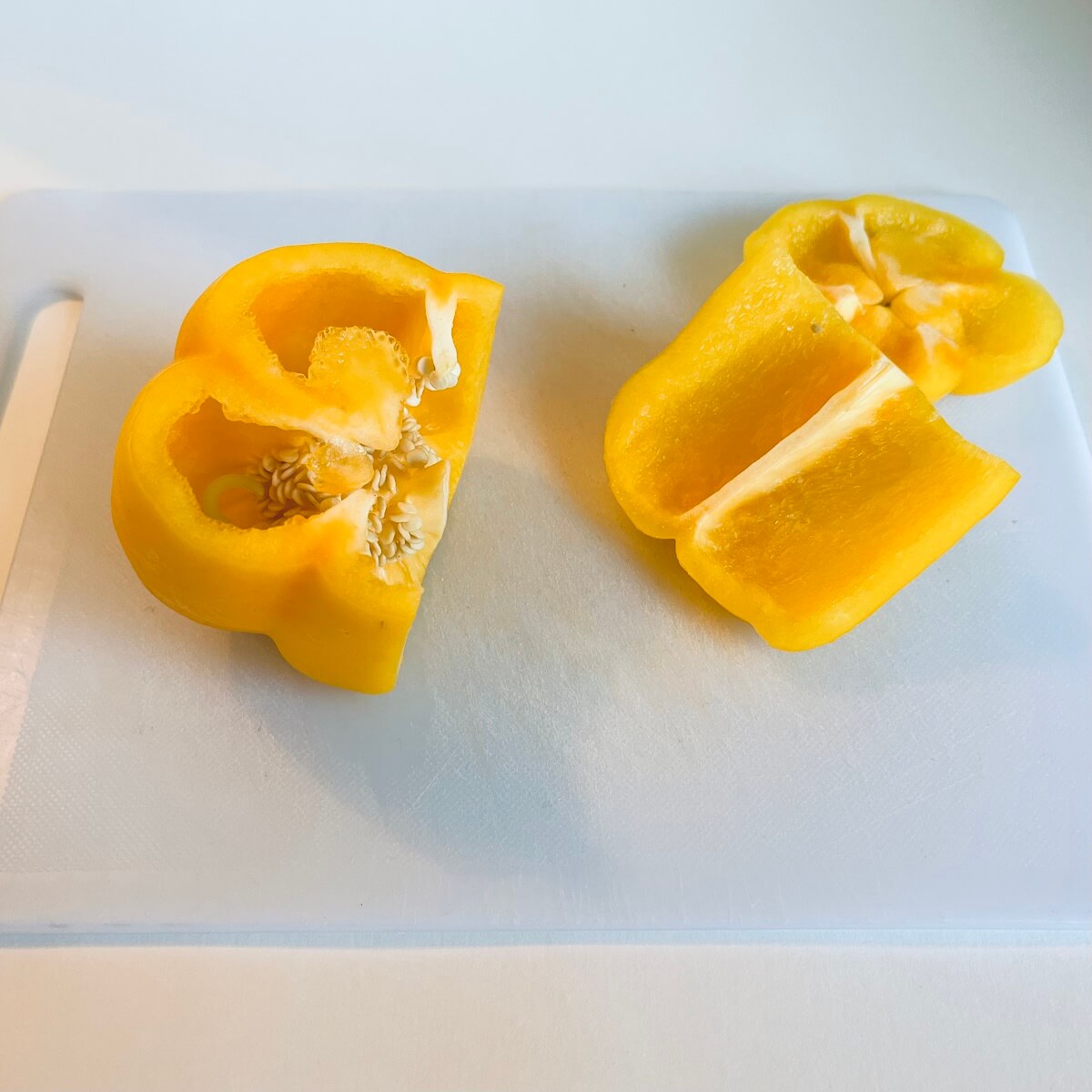 A yellow pepper on a cutting board with two slices cut.