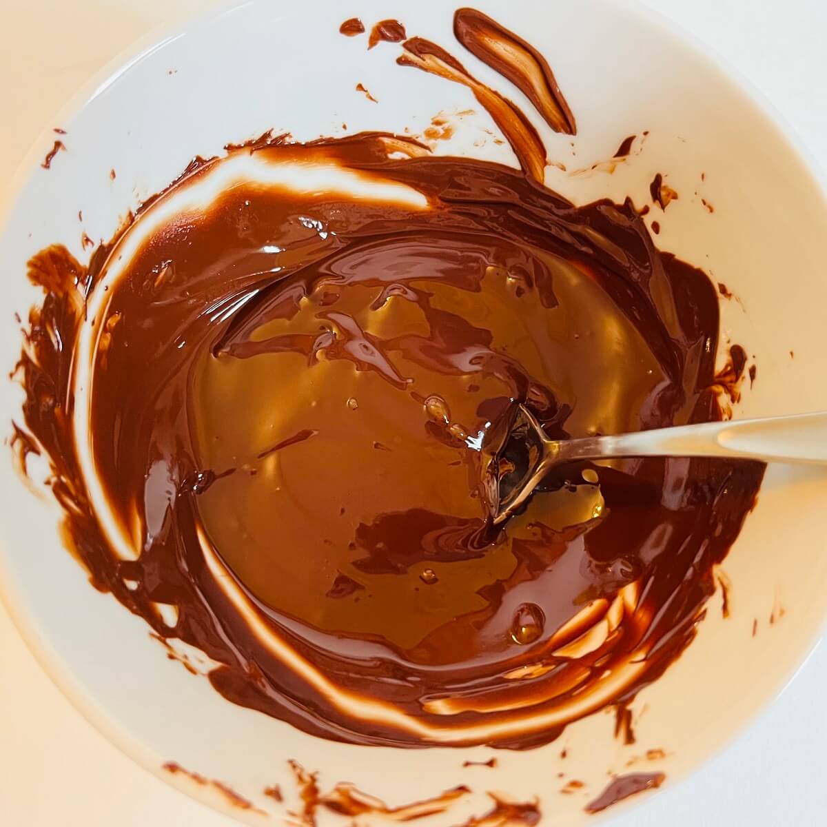 Melted chocolate chips in a white bowl with a spoon.