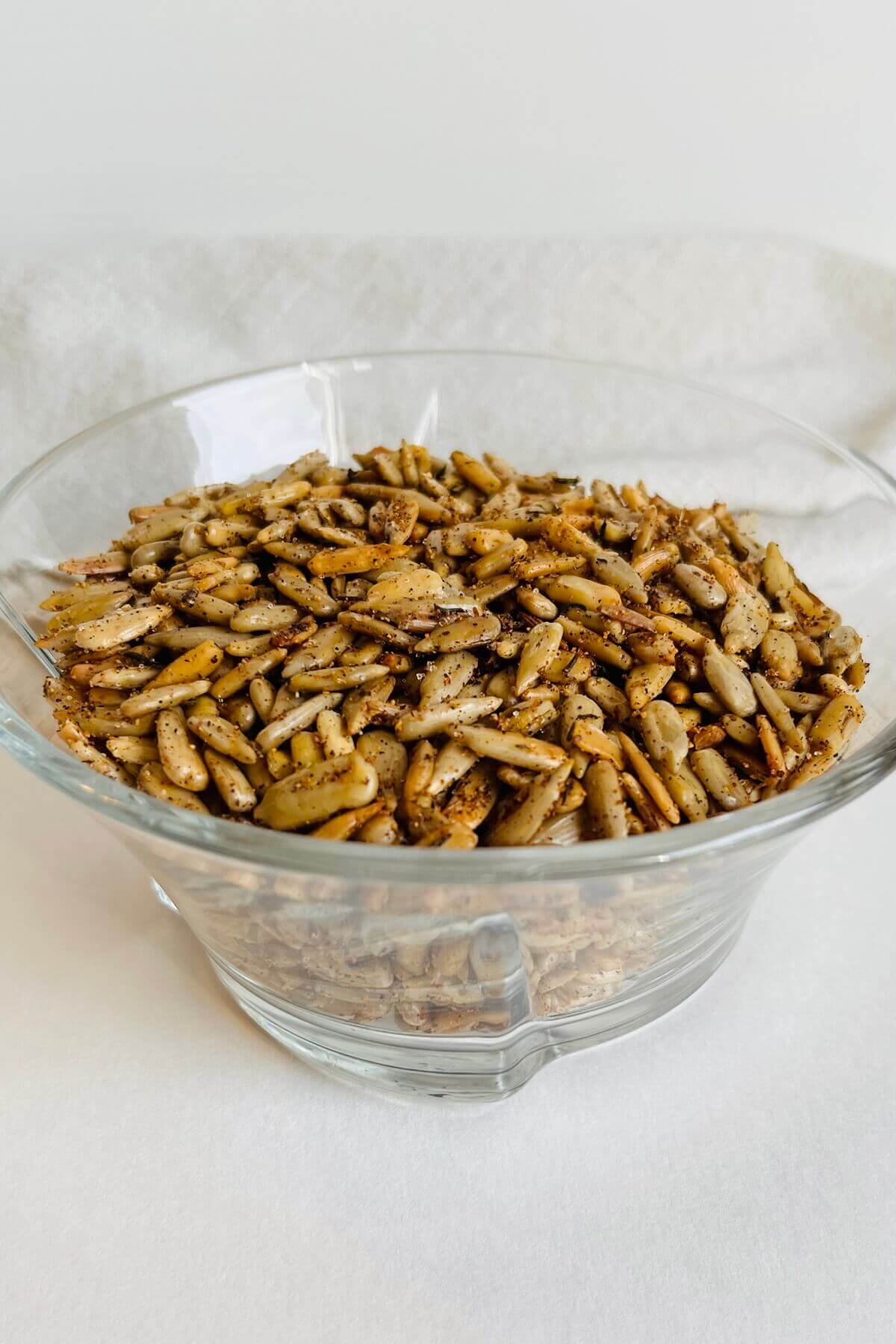 A glass bowl of toasted sunflower seeds in front of a linen napkin.