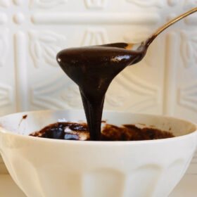 Tahini frosting dripping from a stainless steel spoon.