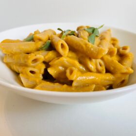 A bowl full of noodles smothered in sweet potato pasta sauce.