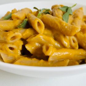 A white bowl full of pasta smothered in an orange sauce.