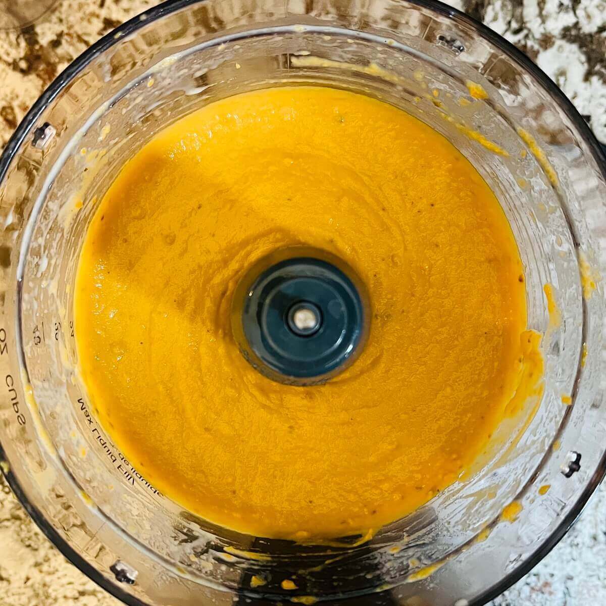 A thick orange colored sauce in a food processor.